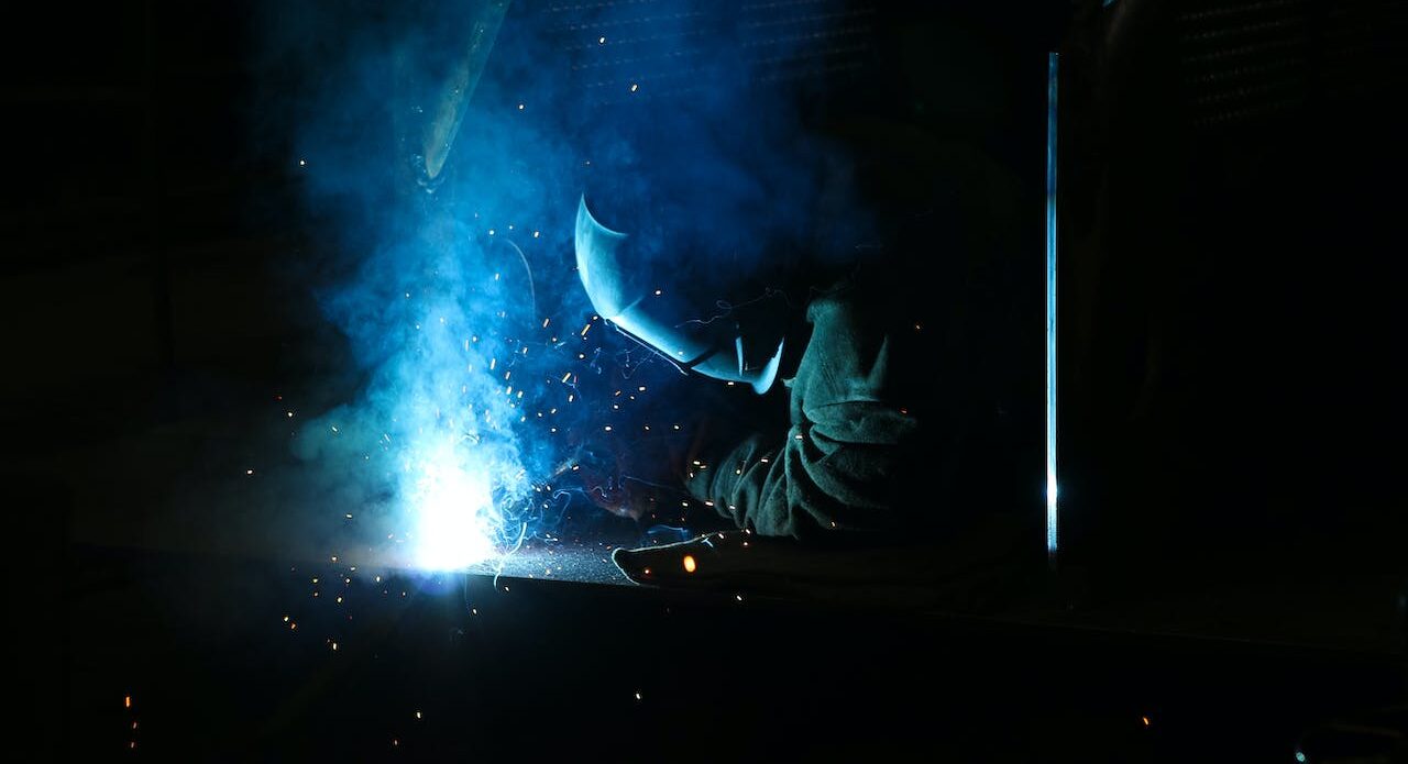 Darkened view of a person in a welding mask, alight by the glow of the welding metal, representing labour grievances and arbitrations in Windsor-Essex County