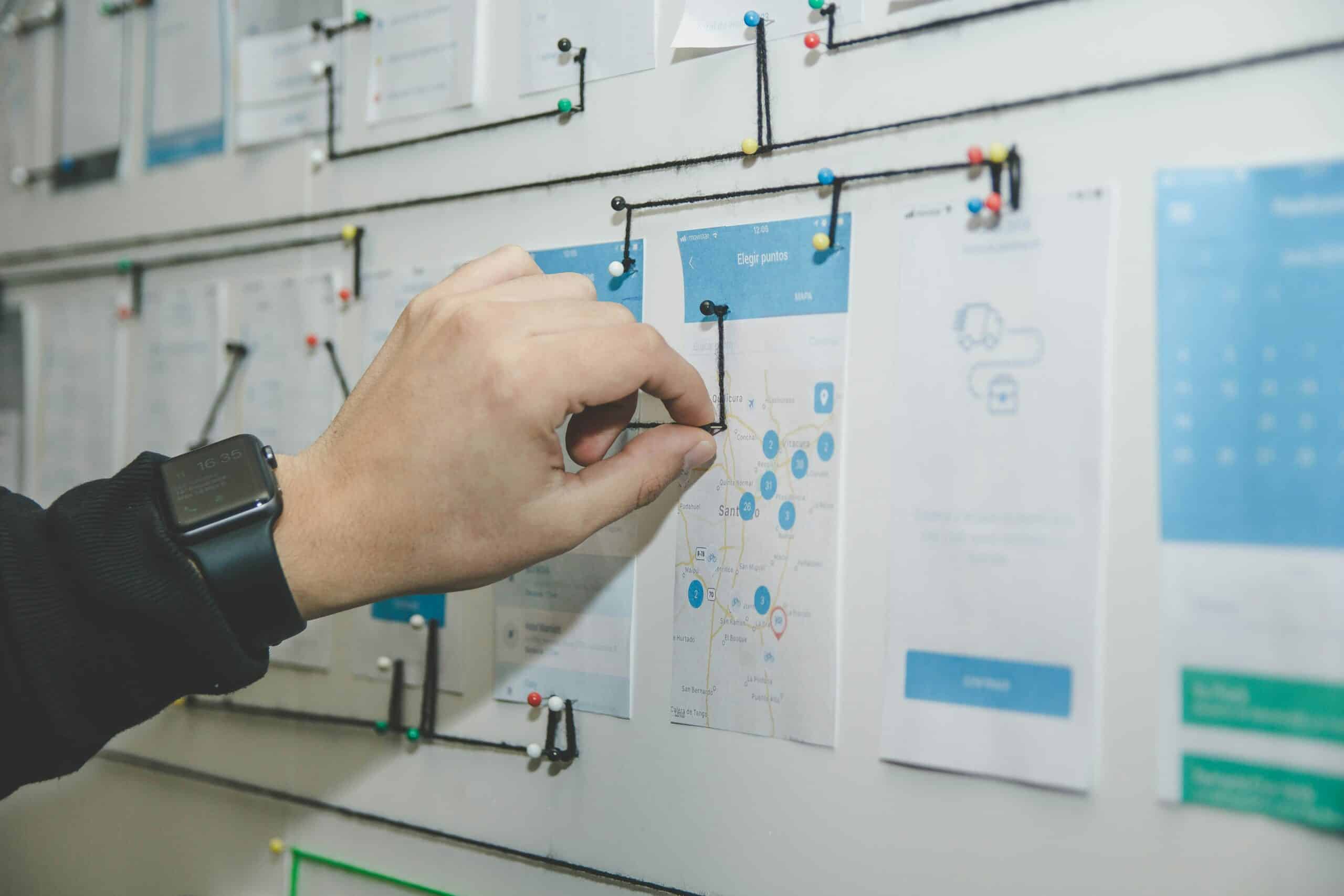 A person's hand attaching threads between planning documents hung on a wall, representing planning a startup business enterprise in Ontario