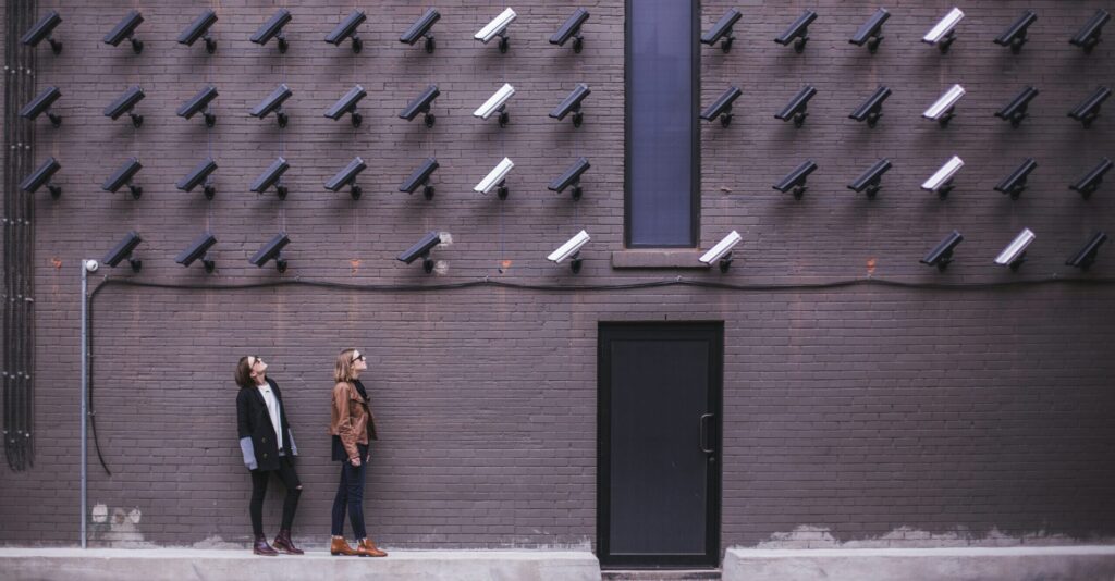 Two women looking up at a grey alley wall covered in surveillance cameras, representing employee privacy in the workplace