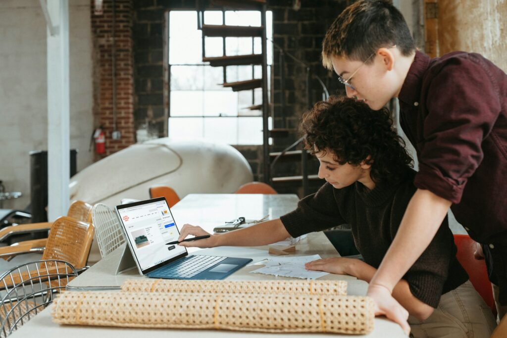 A man and woman leaning over a laptop at a small business's workshop, representing selling a business in Windsor-Essex