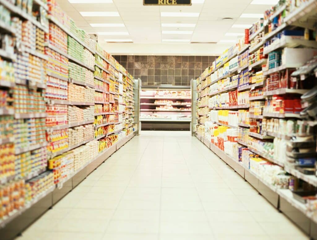 View looking down centre of grocery store aisle with full stocked shelves on either side, representing consumer protection laws in Canada