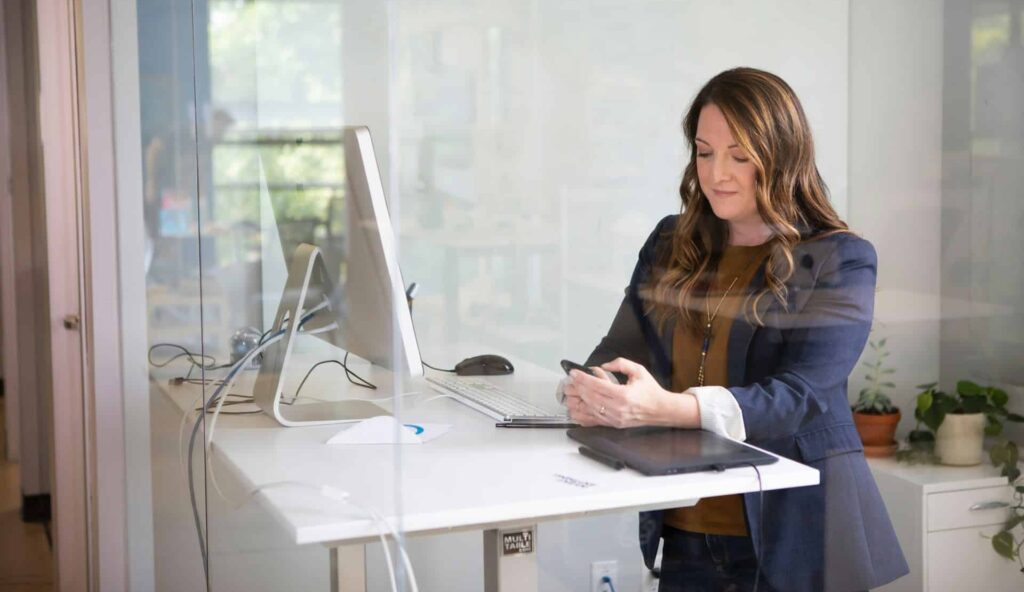 Female business person working at a standing desk and looking at her cell phone, representing professional Limited Liability Partnerships (LLP) in Ontario