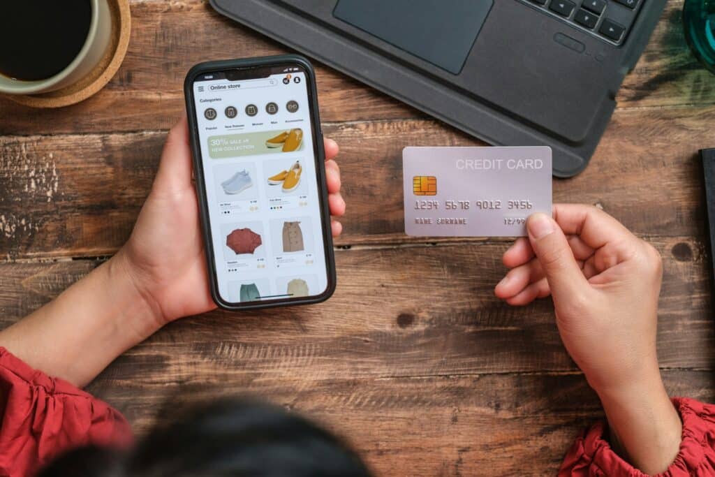 Close up of a person holding their cell phone with the screen showing an online clothing store in one hand, and a credit card in the other hand, representing e-commerce laws in Ontario