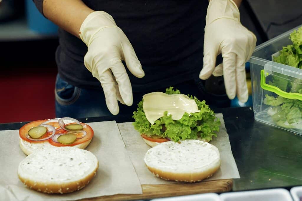 a person wearing gloves making a sandwhich