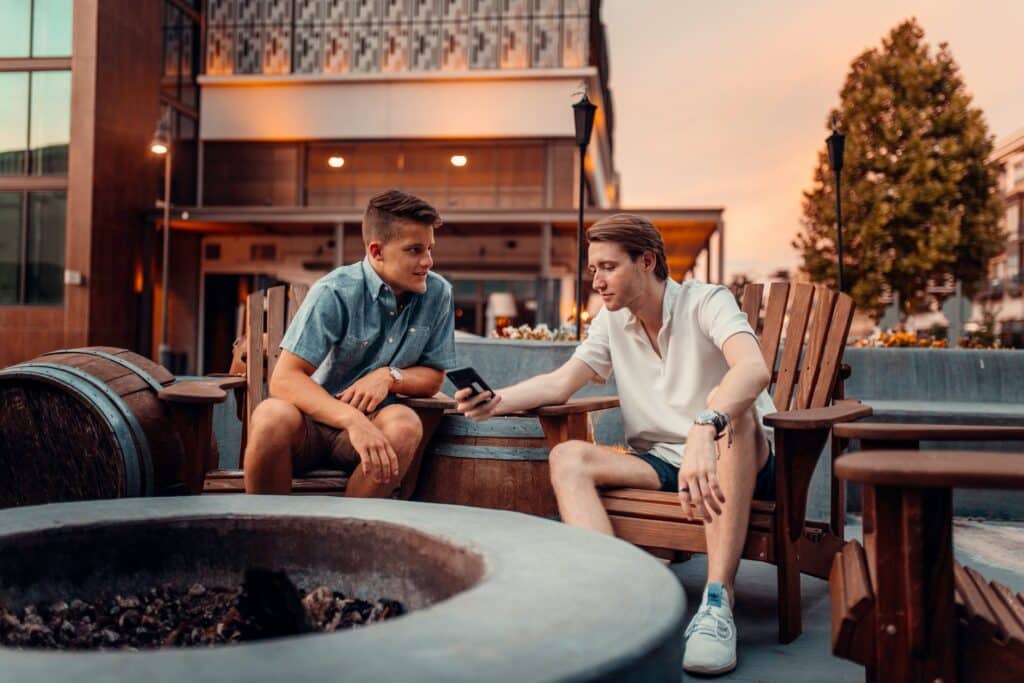 Two men sitting by a firepit, looking at a cell phone together, representing off-duty text messaging and workplace sexual harassment.