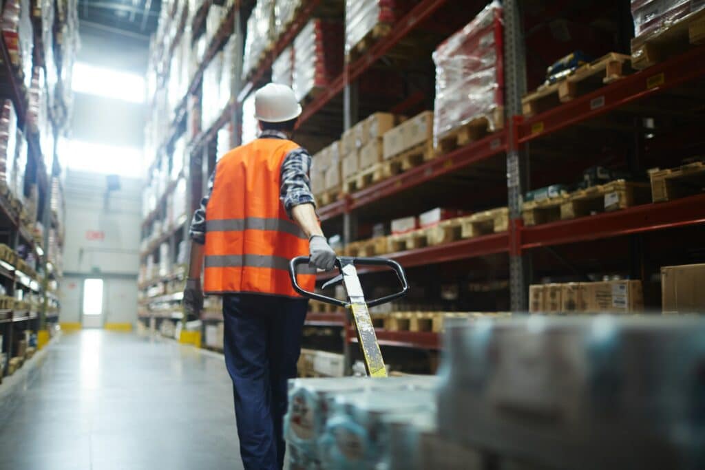 A worker wearing a helmet and safety vest pulling a trolley of supplies through a warehouse, representing tendering and RFP procurement processes.