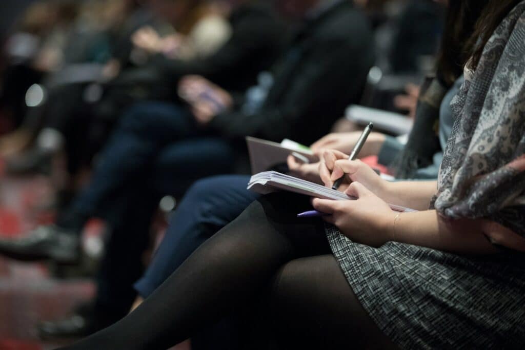 A close-up view of an audience member taking notes in a notebook during a professional event. The setting suggests a legal or business conference discussing complex topics, such as the nuances of constructive dismissal.