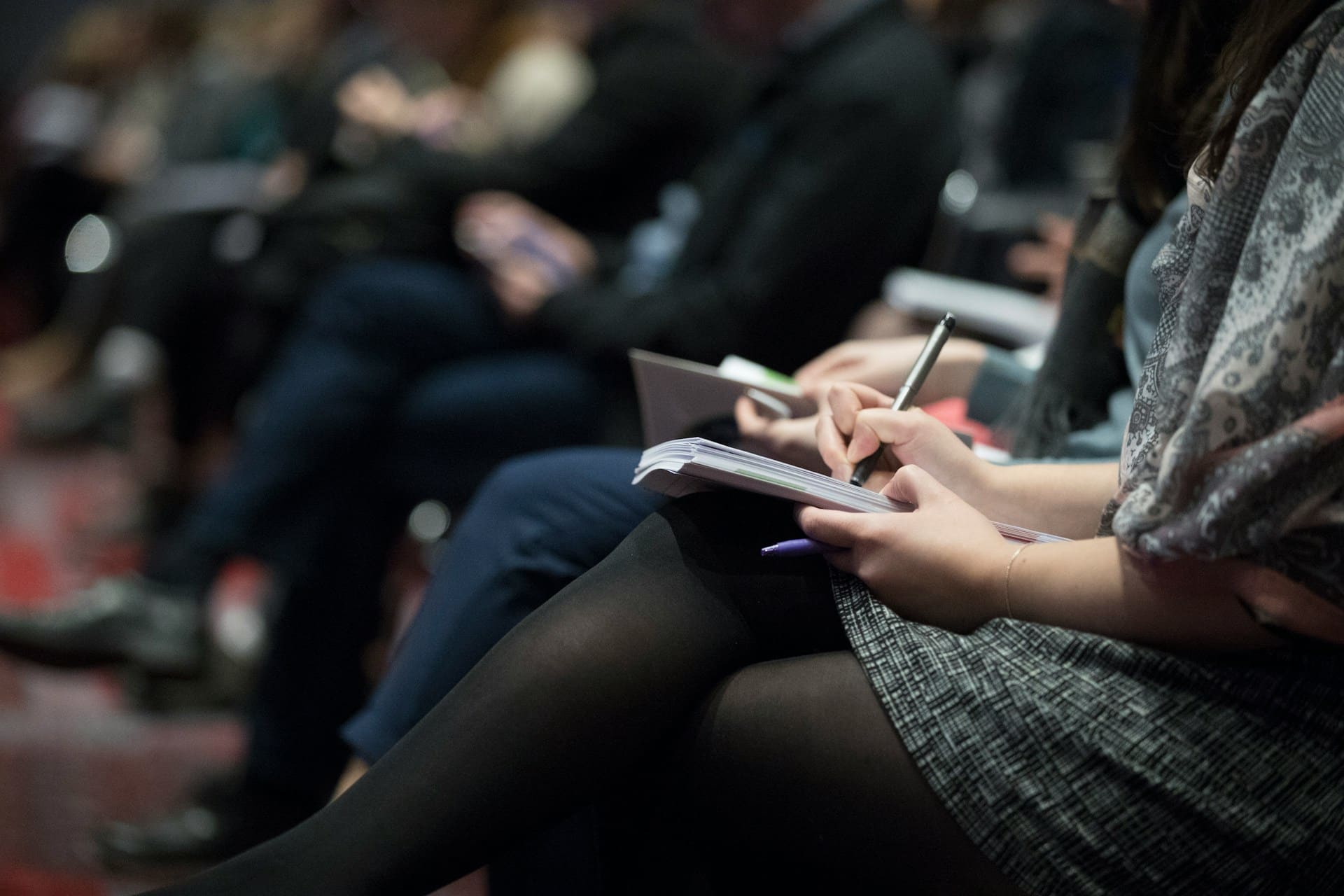 A close-up view of an audience member taking notes in a notebook during a professional event. The setting suggests a legal or business conference discussing complex topics, such as the nuances of constructive dismissal.