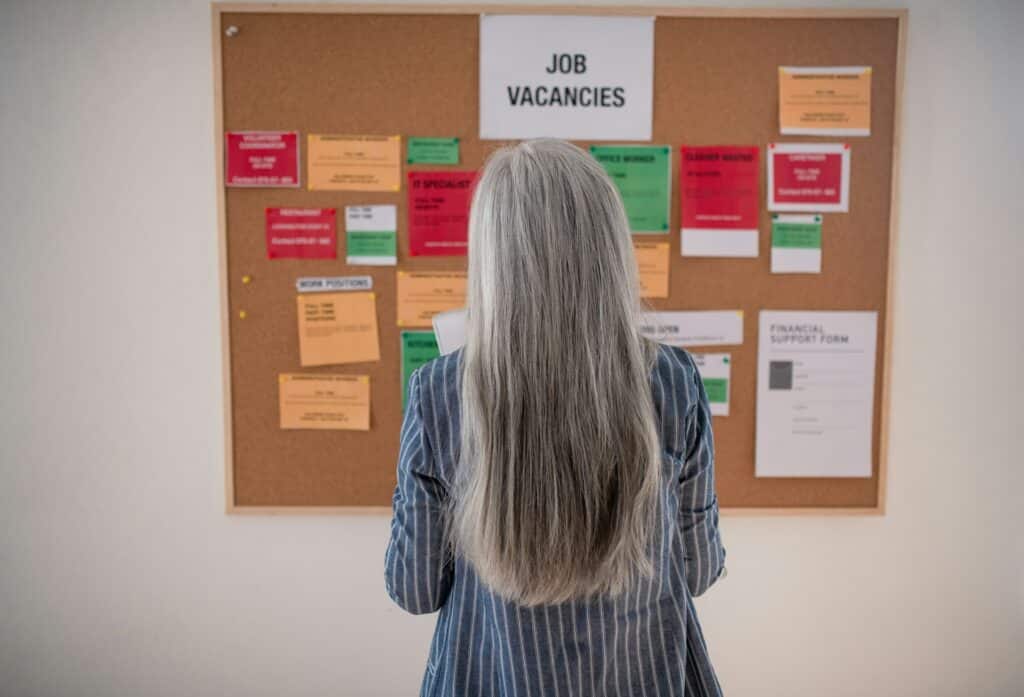 A woman with long grey hair standing in front of a job posting board, representing the new hiring and pay transparency rules coming into effect in Ontario in 2026