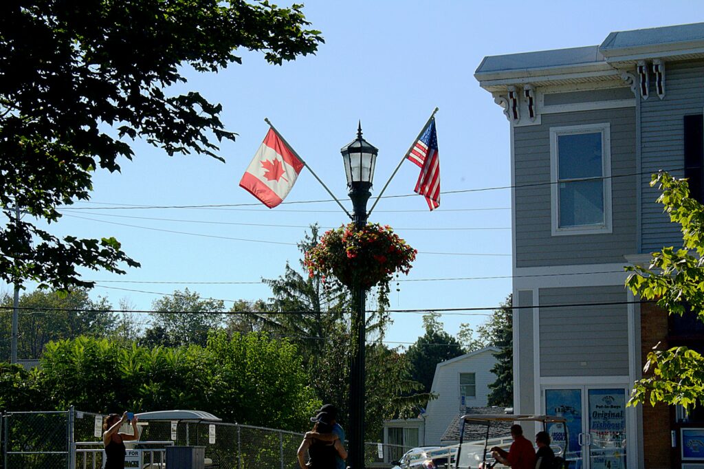 A photo of a Canadian and United States flag on a light pole with a flower basket dipicting what U.S. companies need to know about hiring Canadian employees.