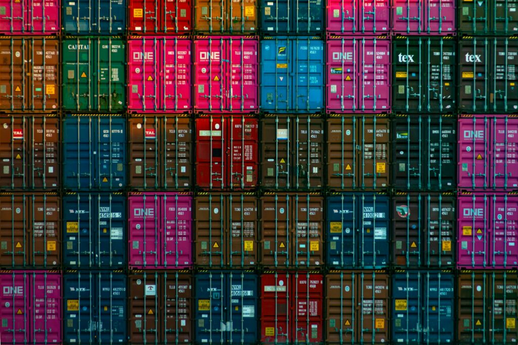 Multicoloured shipping containers stacked in a grid, representing allocation of tariffs in Windsor-Essex, Ontario, commercial contracts.